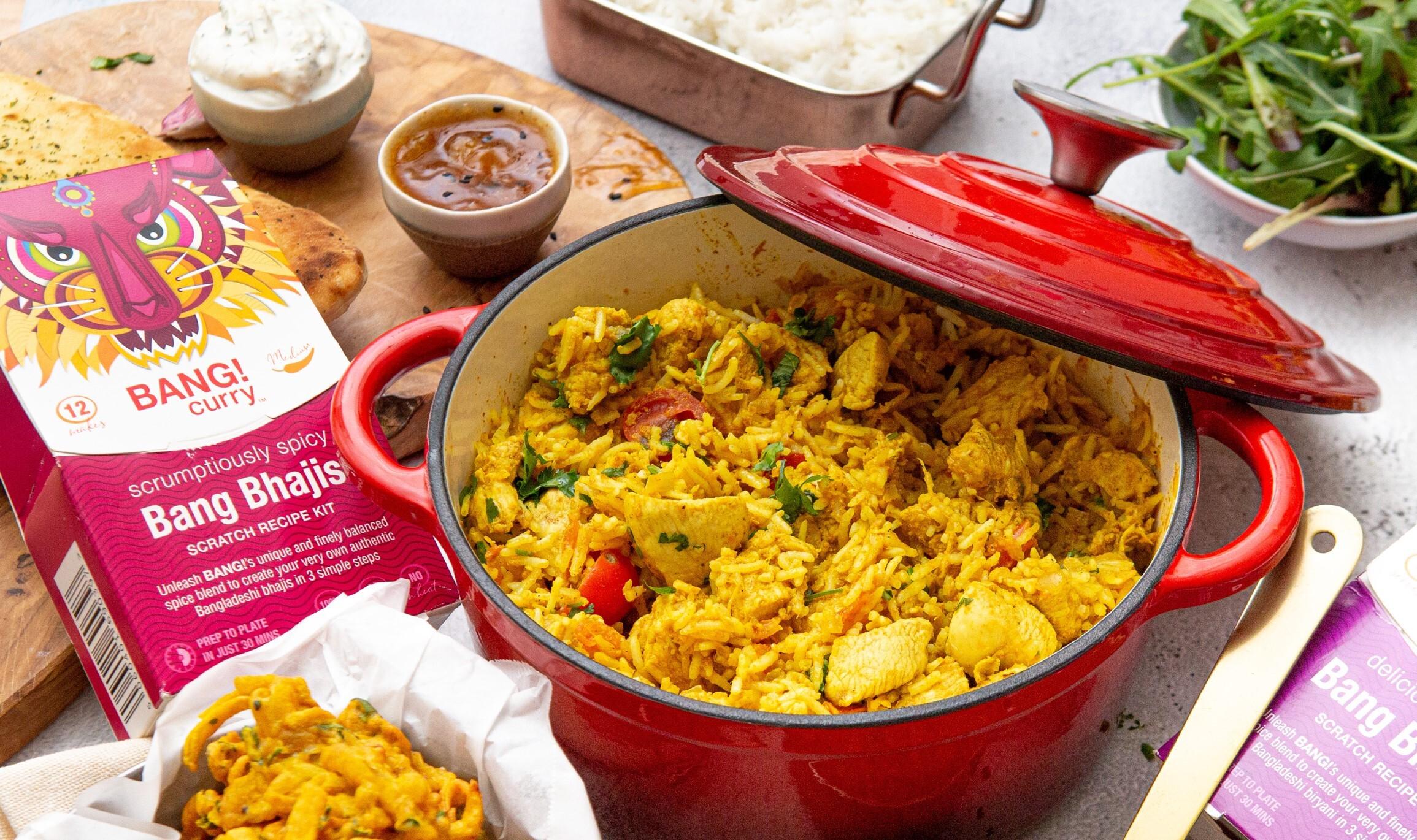 Image of red cooking pot filled with flavourful rice dish sitting next to a curry product kit by Bang Curry.